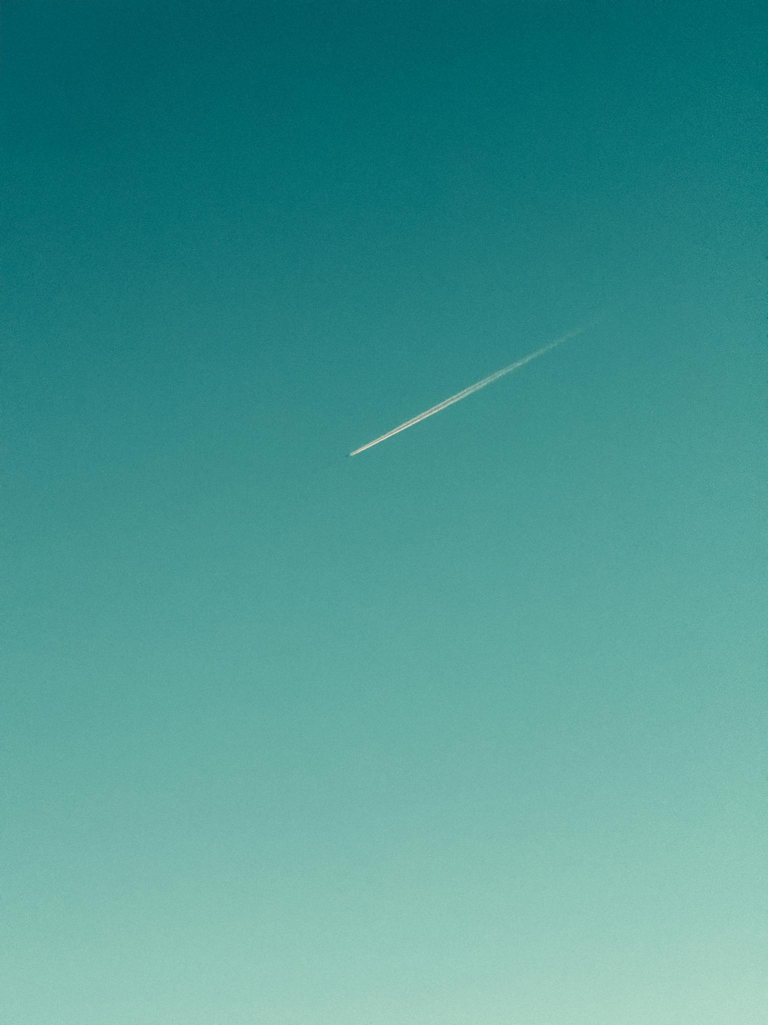 A sleek jet contrail streaks across a clear blue sky, offering a serene minimalist view.